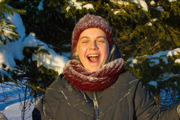 Foto van een meisje op de achtergrond van besneeuwde dennenpootjes. pluizige sneeuw. gebreide rode muts. - Foto, afbeelding