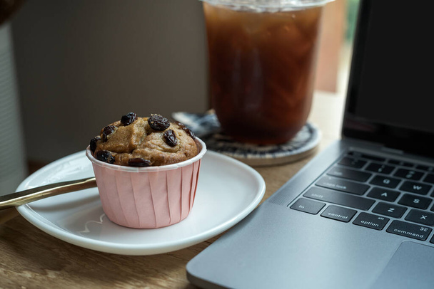 Close-up of ice coffee in cup mug and Homemade Banana cup cake with keyboard laptop computer on wood desk office desk in coffee shop at the cafe,during business work concept - Photo, image