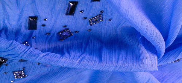 Seidenmuster, blauer Stoff mit aufgeklebten facettierten Schmucksteinen. Textur Hintergrund mit hellen bunten Steinen, Textur Hintergrunddesign - Foto, Bild