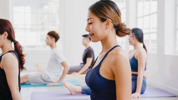 Young Asian sporty attractive people practicing yoga lesson with instructor. Asia group of women exercising healthy lifestyle in fitness studio. Sport activity, gymnastics or ballet dancing class. - Photo, Image