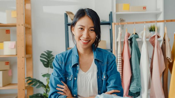 Portret van de jonge Aziatische dame mode-ontwerper gevoel vrolijke glimlach, armen gekruist en op zoek naar camera tijdens het werk kledingwinkel in het thuiskantoor. Eigenaar van een klein bedrijf, concept voor online marktlevering. - Foto, afbeelding