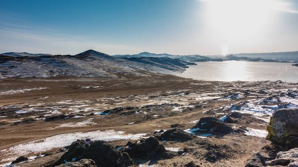 O lago congelado é cercado por montanhas. Terra coberta de neve. O sol brilha no gelo. Não há pessoas. Céu azul claro, dia de inverno. Baikal. - Foto, Imagem