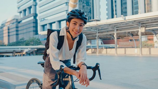 Femme d'affaires asiatique aller travailler au stand de bureau et souriant sac à dos regarder la caméra avec vélo sur la rue autour du bâtiment sur une ville. Transport à vélo, Transport à vélo, Concept de navetteur d'affaires. - Photo, image