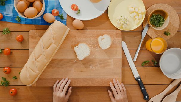 Jonge Aziatische vrouw chef-kok verspreid boter op rustieke roggebrood met metalen mes op houten plank op keukentafel in huis. Verse zelfgemaakte broodproductie, Gezond eten en traditionele bakkerij. Bovenaanzicht opname. - Foto, afbeelding