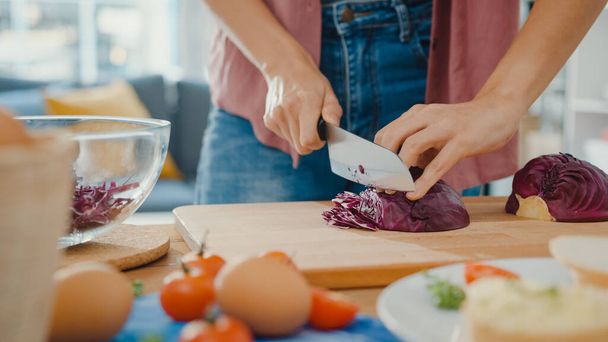 Hand of young Asian woman chef hold knife cutting Red Chinese cabbage on wooden board on kitchen table in house. Cooking vegetable salad, Lifestyle healthy food eating and traditional natural concept. - Photo, Image