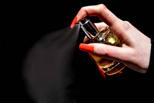 mão elegante com unhas vermelhas pulveriza um perfume em um backgroun preto - Foto, Imagem
