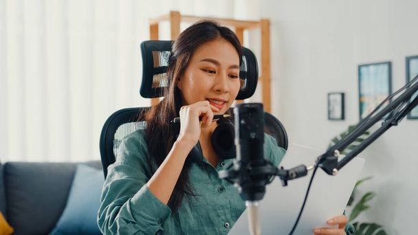 Atrakcyjna azjatycka dziewczyna rekord podcast używać mikrofonu trzymać papier tworzenie treści do audio blog rozmowy i praktyki do tematu przeglądu w jej pokoju. Dodać podcast audio z domu, Koncepcja sprzętu dźwiękowego. - Zdjęcie, obraz
