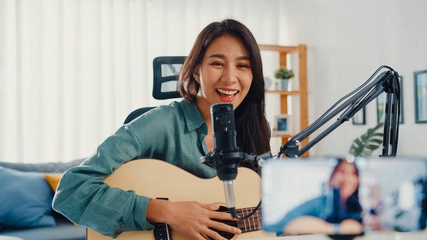 Подростковая азиатка, влияющая на гитарную музыку, использует запись микрофона со смартфоном для онлайн-аудитории. Женщина подкастер сделать аудио подкаст из ее домашней студии, Оставайтесь дома концепции. - Фото, изображение