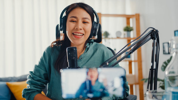 Teenage Asia girl influencer use microphone wear headphone record content with smart phone for online audience listen at house. Student female podcaster make audio podcast from her home studio. - Fotó, kép