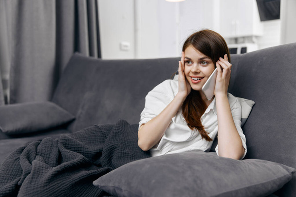 donna felice che parla al telefono sul divano nella stanza e un plaid sulle gambe - Foto, immagini