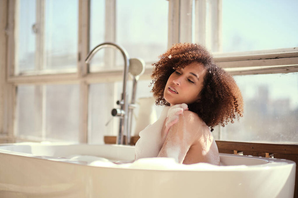Mosolygó és pihentető afro-amerikai nő fürdik egy kádban tele habbal. Csodálatos volt. életmód emberek koncepció - Fotó, kép