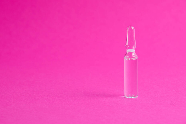 Ampolla con medicina sobre fondo de papel rosa. Medicina en segundo plano con espacio de copia - Foto, imagen
