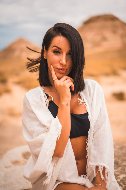 Sensual look of a young brunette Caucasian girl in a white dress sitting in a beautiful desert - Fotoğraf, Görsel