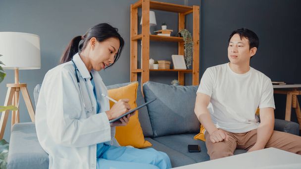 Young Asia female professional physician doctor using digital tablet sharing good health test news with happy male patient sit on couch in house. Medical insurance, Visit patient at home concept. - Valokuva, kuva