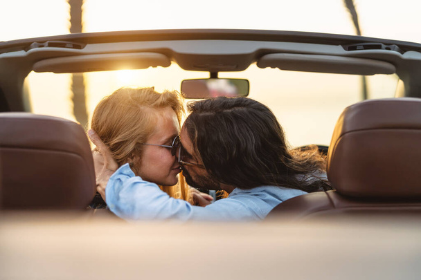 Happy couple kissing in convertible car - Romantic people having tender moment during road trip in tropical city - Love relationship and youth vacation lifestyle concept - Фото, зображення