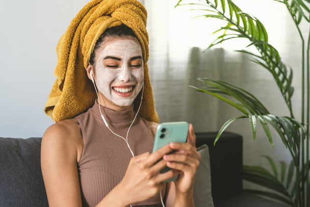 Young woman using mobile smartphone while having skin care spa day at home - Photo, Image