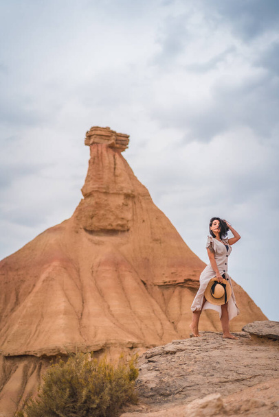 Brunette Caucasian girl in an explorer outfit with a white dress and a straw hat in a beautiful desert on a cloudy afternoon - Fotó, kép