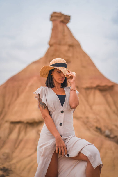 Sensual gazes of a brunette Caucasian girl in an explorer outfit with a white dress and a hat in a desert on a cloudy afternoon - Фото, изображение