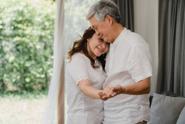 Asiatisches älteres Paar tanzt zusammen, während es zu Hause Musik im Wohnzimmer hört, süßes Paar genießt den Moment der Liebe, während es zu Hause entspannt Spaß hat. Lifestyle Senioren Familie entspannen zu Hause Konzept. - Foto, Bild