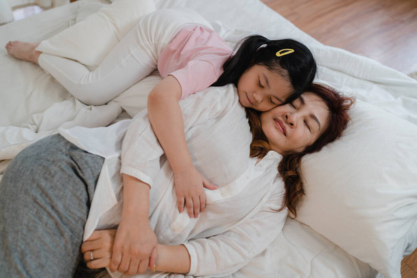 Aziatische oma slaapt thuis. Senior Chinees, oma gelukkig ontspannen met jonge kleindochter meisje kussen wang voor wakker liggen op bed in de slaapkamer thuis 's nachts concept. - Foto, afbeelding