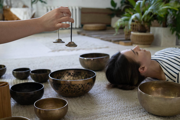 Woman practice sound massage, Tibetan singing bowls treatment. Oriental meditation tradition concept - Photo, Image