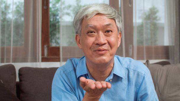 Asian senior man video call at home. Asian senior older Chinese male using mobile phone video call talking with family grandchild kids while lying on sofa in living room at home concept. - Photo, Image