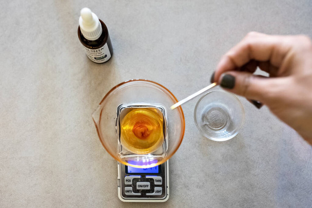 Een zeepmaker weegt aromatische oliën voor het maken van cosmetica op keukenschaal. Thuis spa. Kleine bedrijven. - Foto, afbeelding