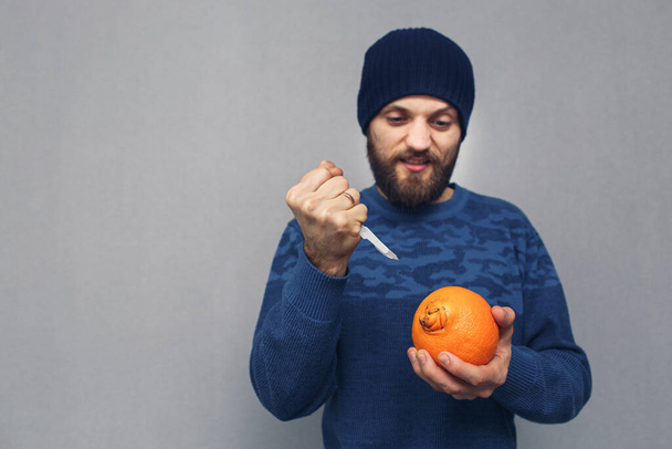Wütender bärtiger Mann will einen großen Nabel einer Orange mit dem Skalpell ausschneiden, das Konzept von Hämorrhoiden oder proktologischen Erkrankungen. - Foto, Bild