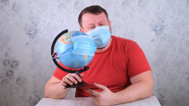 man is sad about the illnesses on the plan and the lack of travel. male looks globe in protective mask and pandemic vaccine. Corona virus treatment concept, injection, clinical trials during a - Footage, Video