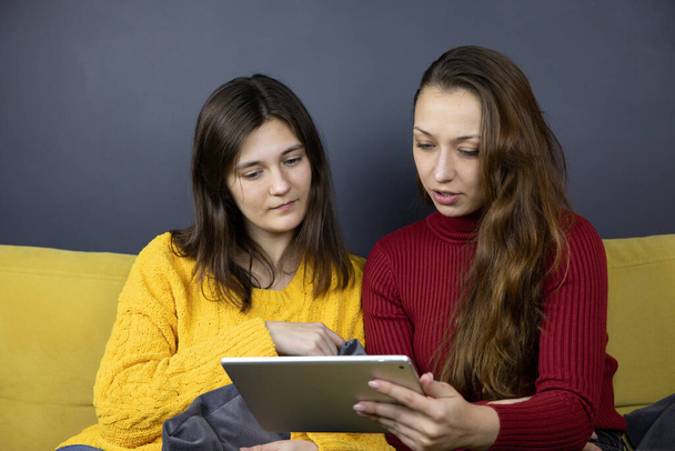 dos chicas bonitas utilizando la tableta y el Internet para las compras de sofá en el sitio de comercio electrónico - Foto, imagen