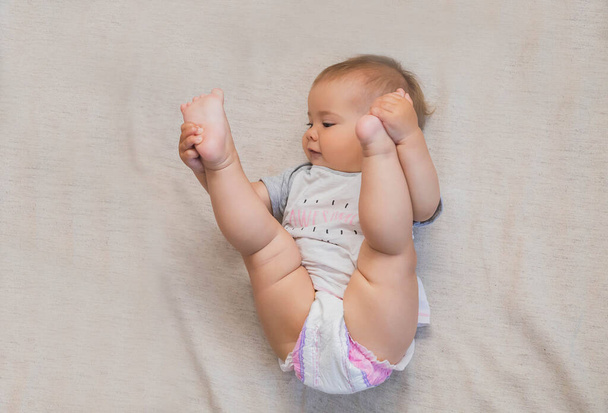 όμορφο μωρό σε μια πάνα σήκωσε τα πόδια του στο κεφάλι του - Φωτογραφία, εικόνα