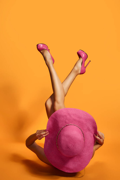 Nainen vaaleanpunaisissa korkeakorkoisissa kengissä ja olki kesähattu lattialla jalat ylhäällä. studio, keltainen tausta - Valokuva, kuva