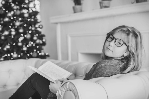Bella ragazza che legge un libro sul divano vicino all'albero di Natale - Foto, immagini