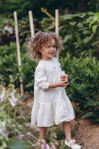 beautiful little girl with curly hair posing for photo walking among the flowers in nature - Foto, afbeelding
