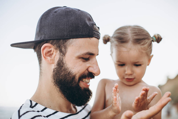 family portrait of stylish bearded father with cute daughter spending time playing by the sea - Foto, Imagen