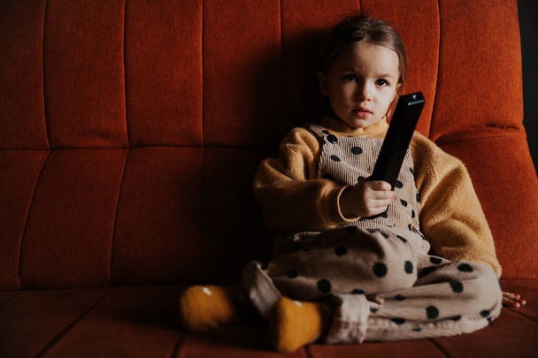 little girl watching tv lying on the couch with a remote control in hand - 写真・画像