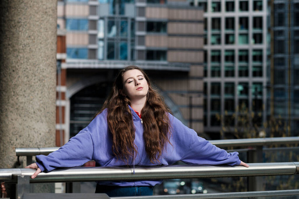 Retrato de una mujer joven en un sudor con capucha púrpura, entorno financiero.Imagen relajada en el distrito financiero de Londres. - Foto, Imagen