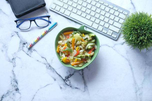 vrchní pohled na misku čerstvé vařené zeleniny na kancelářském stole - Fotografie, Obrázek