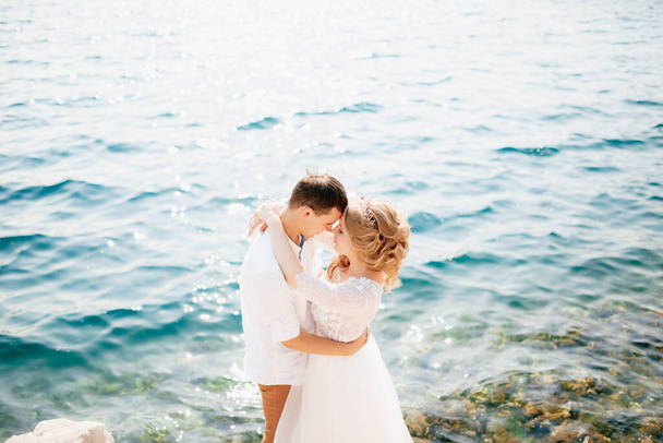 De bruid en bruidegom omhelzen de rotsachtige kust en staan op het punt om te kussen.  - Foto, afbeelding
