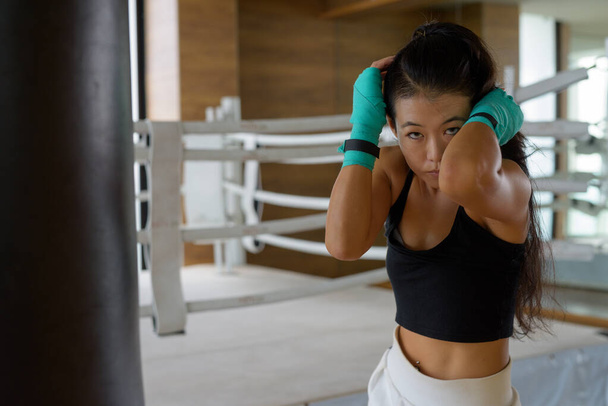 Güzel genç Asyalı kadın boksörü tekmeliyor. Spor salonunda egzersiz yapmaya hazır. - Fotoğraf, Görsel