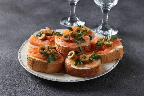 Canapes of salted salmon, green olives and parsley on croutons of white bread on dark gray background. Festive snack. - Photo, Image