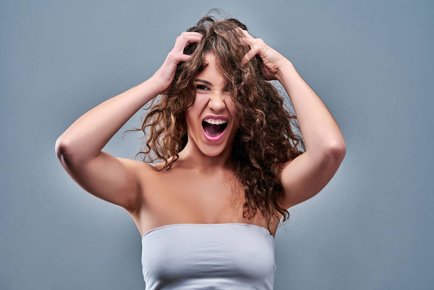 Portrait of a frustrated angry woman screaming out loud and pulling her hair out isolated on the gray background. - Photo, image