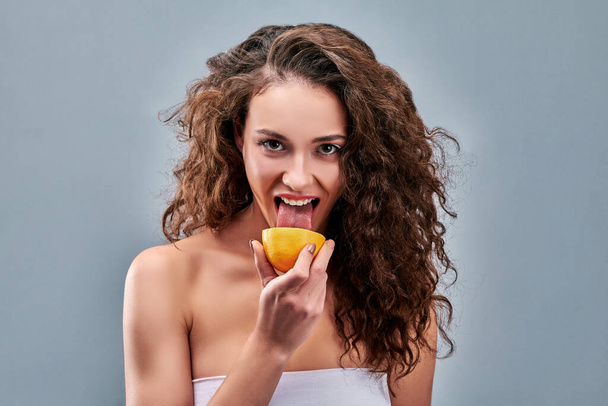 Girl licks a half of orange on grey isolated background. - Photo, image
