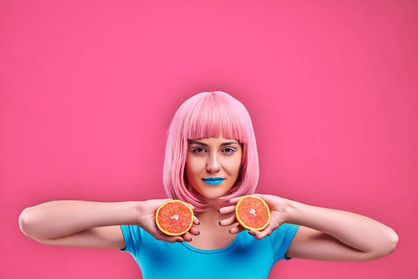 Happy young woman holding oranges halves on a pink background. Copy space - Zdjęcie, obraz