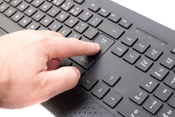 Το δάχτυλο πατά το πλήκτρο enter σε ένα ασύρματο μαύρο προσωπικό πληκτρολόγιο υπολογιστή. - Φωτογραφία, εικόνα