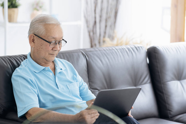 老人はデジタルタブレットでニュースを読んでいる。自宅でポータブルコンピュータを使用して成熟した男性. - 写真・画像