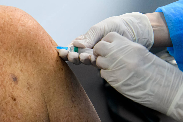 Close up das mãos de um profissional de saúde que vacina um idoso com uma vacina contra o coronavírus.  - Foto, Imagem