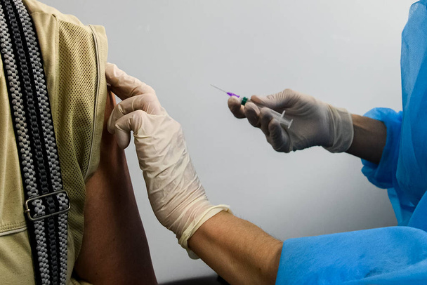 Nahaufnahme aus den Händen eines Gesundheitspersonals, das einen älteren Menschen mit einem Coronavirus-Impfstoff impft. Hände in Schutzhandschuhen halten eine Spritze mit dem Impfstoff in der Hand. Hochwertiges Foto - Foto, Bild
