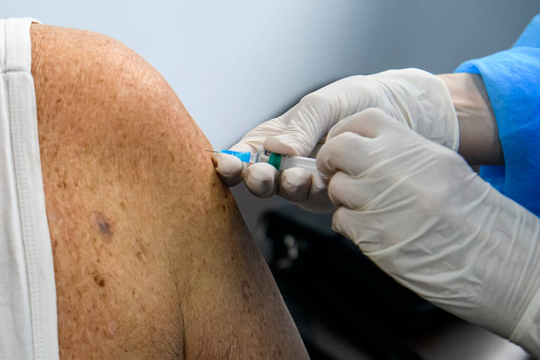 Gros plan des mains d'un travailleur de la santé qui vaccine une personne âgée avec un vaccin contre le coronavirus. Les mains dans les gants de protection tiennent une seringue avec le vaccin. Photo de haute qualité - Photo, image