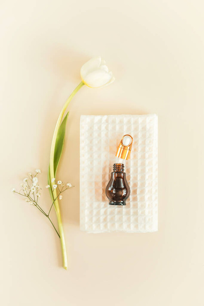 Minimalistic, spa natural, cosmetic composition with white towel, glow serum bottle and tulip on a light background. Wellness, home skin care and relax treatment concept. Top view - Photo, image